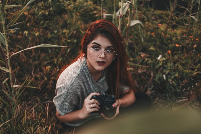 Frau sitzt in der Natur mit einer Foto-Kamera in der Hand